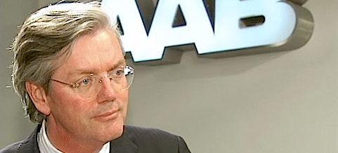 En man i kostym och slips pratar inför en kamera. (AI text)