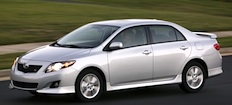 En vit Toyota Corolla kör nedför en väg. (AI text)