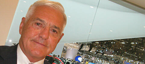 En man i kostym och slips står framför en bil. (AI text)