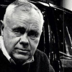 En man i en svart bil med en skylt på den. (AI text)