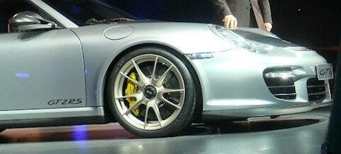 En man och kvinna står bredvid en silverfärgad Porsche 911 GTS. (AI text)
