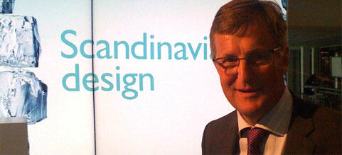 En man i kostym och slips står framför en skärm med texten "Skandinavisk design". (AI text)