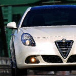 En vit Alfa Romeo kör över en bro. (AI text)