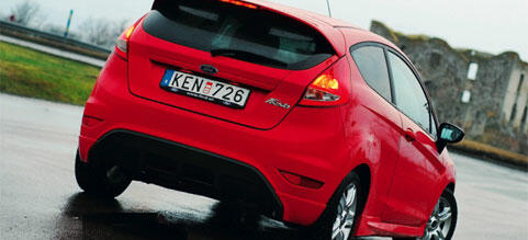 En röd Ford Fiesta kör nedför en blöt väg. (AI text)