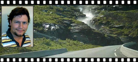 En man kör nedför en väg med ett vattenfall i bakgrunden. (AI text)