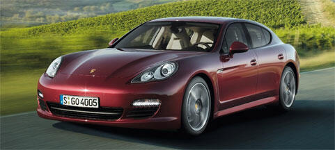En röd Porsche Panamera kör nedför en väg. (AI text)