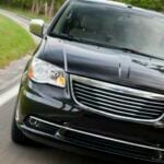 En svart Chrysler Town & Country kör fram på en landsväg. (AI text)