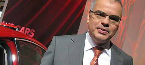 En man i kostym står bredvid en röd bil. (AI text)