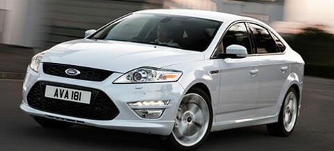 En vit Ford Mondeo kör nerför vägen. (AI text)