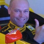 En man i en gul racerbil ger en vink med tummen upp. (AI text)