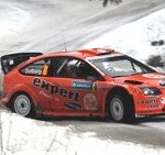 En Ford Focus från Rally-VM kör ner en snöig väg. (AI text)