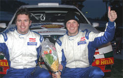 Två personer poserar med blommor framför en rallybil. (AI text)