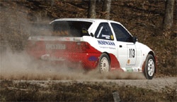 En rallybil kör nedför en grusväg. (AI text)