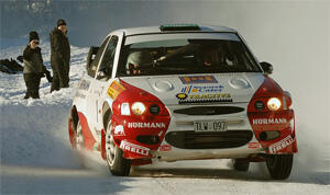 En rallybil körer nedför en snöig väg. (AI text)