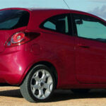 En röd bil parkerad på en strand. (AI text)