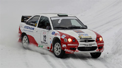 En rallybil kör nedför en snöig backe. (AI text)