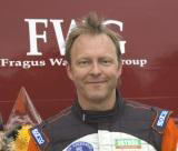 En man i en racerdräkt står bredvid en bil. (AI text)