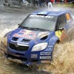 En rallybil körs genom en blöt och smutsig yta. (AI text)