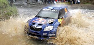 En rallybil körs genom en blöt och smutsig yta. (AI text)