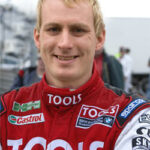 En racerförare poserar med armbågarna korsade. (AI text)