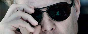 En man i solglasögon tittar på sin mobiltelefon. (AI text)