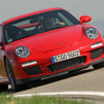 En röd Porsche 911 GTS kör längs en väg. (AI text)