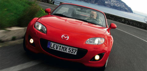 En röd Mazda MX-5 roadster kör ner en väg. (AI text)