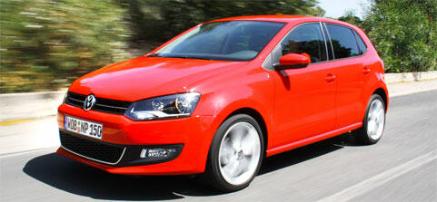 En röd Volkswagen Polo kör nerför en väg. (AI text)
