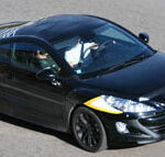 En svart sportbil kör nedför en väg. (AI text)