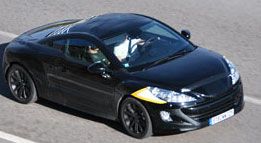 En svart sportbil kör nedför en väg. (AI text)