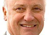 En man i kostym och slips leder glad åt kameran. (AI text)