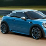 En blå Mini Cooper S kör nerför vägen. (AI text)