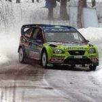 En rallybil körer nedför en snöig väg. (AI text)