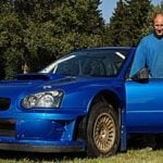 En man står bredvid en blå Subaru WRX STI. (AI text)