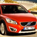 En röd Volvo XC90 kör nerför en väg. (AI text)