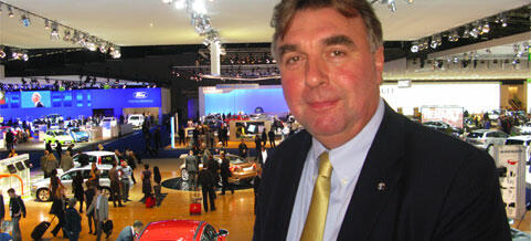 En man i kostym står framför en bil. (AI text)