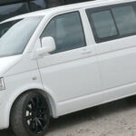 En vit Volkswagen T4-van parkerad framför ett byggnad. (AI text)