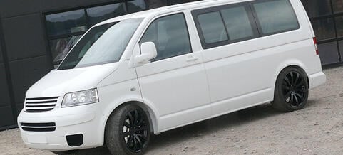 En vit Volkswagen T4-van parkerad framför ett byggnad. (AI text)