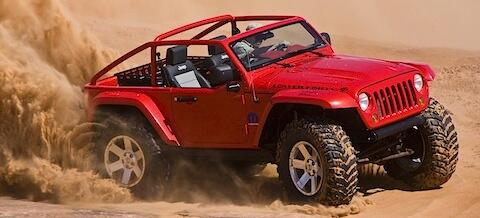 En röd Jeep Wrangler kör genom sanden. (AI text)