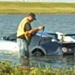 En man står bredvid en bil i vattnet. (AI text)