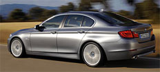 En BMW 5-serie sedan kör nerför vägen. (AI text)