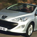 En silverfärgad Peugeot 208 roadster kör ner en väg. (AI text)