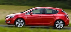 En röd Opel Astra kör nedför en landsväg. (AI text)