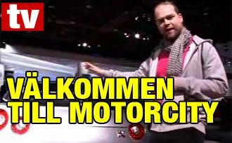 En man står bredvid en bil med texten "Välkommen till Motorcity". (AI text)