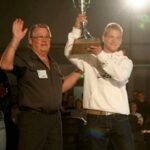 En man höjer upp en trofé. (AI text)