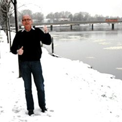 En man står i snön bredvid en flod. (AI text)