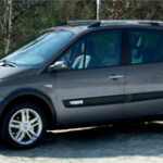 En liten grå bil parkerad på en grusväg. (AI text)