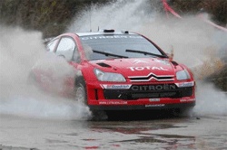 En röd Citroën C3-rallybil kör genom en smutsig, blöt yta. (AI text)