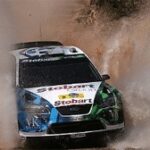 En rallybil kör genom en blöt och smutsig yta. (AI text)