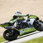 En grön motorcykel rasar nerför en backe. (AI text)